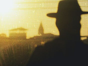 Silhouette man wearing hat against fence