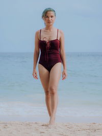 Portrait of young woman wearing swimwear while walking at beach against clear sky