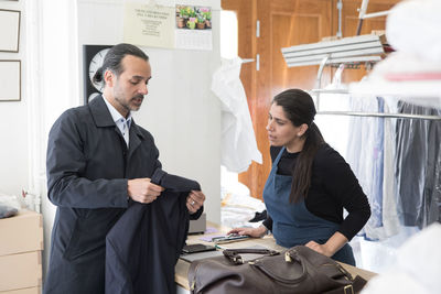 Mature male owner showing suit to female entrepreneur at laundromat