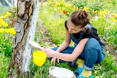 Teenager girl painting tree trunk outdoors