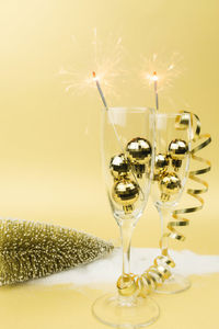 Sparkling wine glasses, sparklers, christmas tree balls, ribbon, gold background