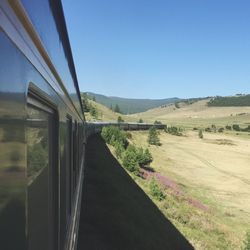 Road passing through field against clear blue sky