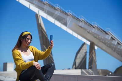 Low angle view of young woman using smart phone against sky