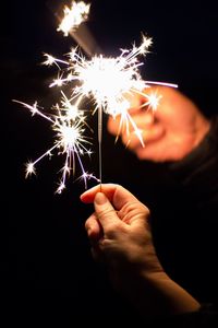 Hands holding sparklers against black background