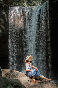 Man sitting on chair against waterfall in forest