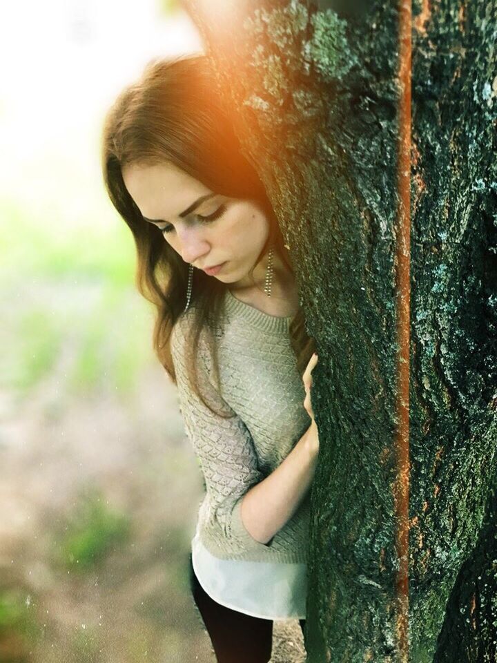 YOUNG WOMAN LOOKING AWAY WHILE TREE TRUNK