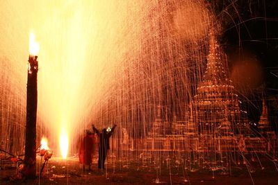 People celebrating with fireworks at temple during night