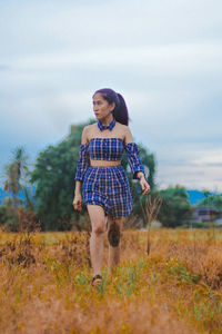 Full length of young woman standing on field against sky
