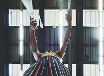 Low angle view of shirtless juggler juggling against illuminated ceiling