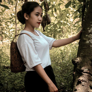 Teenage girl looking away while standing against tree trunk