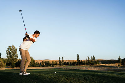 Professional male golf player preparing to hit ball with putter in green field while looking down on summer day