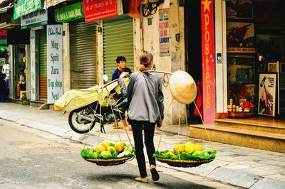 Rear view of female vendor selling fruits on street in city