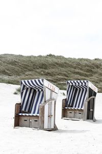 Hooded chairs on beach against clear sky