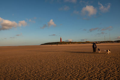 Full length of woman with dog on sand against sky