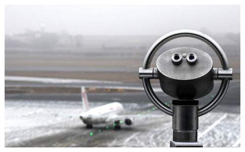 Close-up of coin-operated binoculars against airport runway