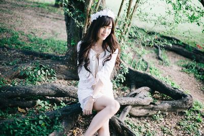 High angle view of young woman wearing tiara sitting by tree in forest