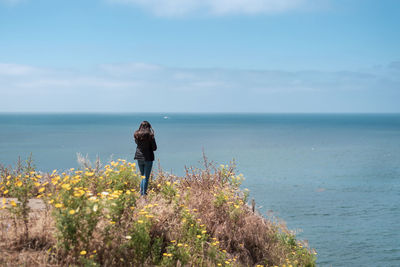 Rear view of woman standing by sea against sky