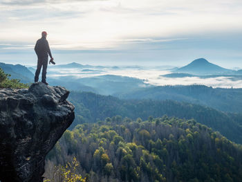 Camera in the hand man tourist standing on rocky edge and looking into landscape. photographer works