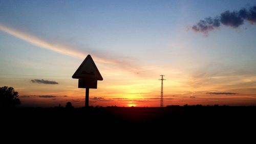 Silhouette signboard on field against sky during sunset