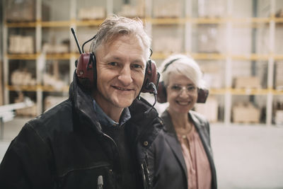 Portrait of smiling businessman with colleague wearing ear protectors at industry