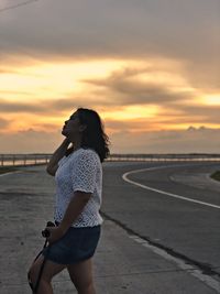 Woman standing on road against sky during sunset