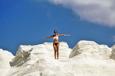 Low angle view of young woman wearing bikini while standing on rock formation against sky during sunny day