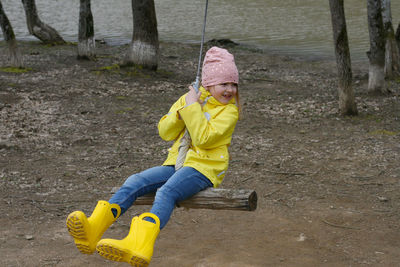 A girl in a yellow jacket and yellow boots swing rides on the background of the lake