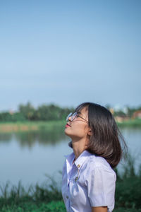 Woman standing by lake against clear blue sky