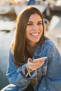 Cheerful woman using phone while sitting outdoors