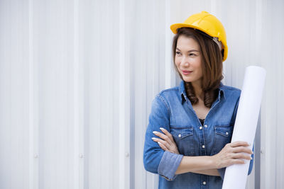 Portrait of smiling young woman standing against wall