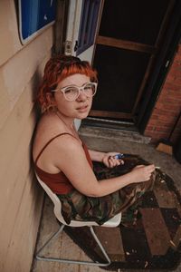 High angle portrait of woman sitting on chair while smoking cigarette at home