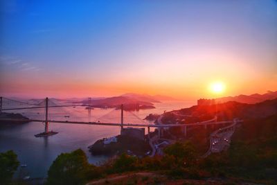 Bridge over cityscape against sky during sunset