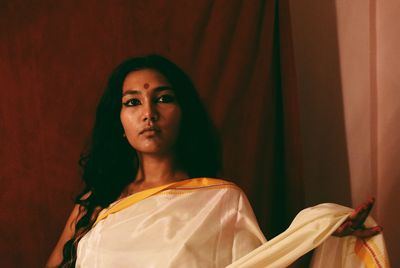 Portrait of young woman in sari standing against curtain