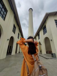 Rear view of woman standing by buildings against sky