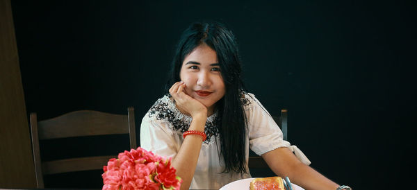 Portrait of smiling woman with breakfast on table sitting against black background