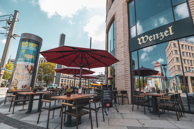 Chairs and tables at restaurant by buildings against sky