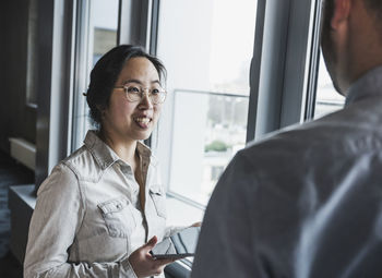 Businesswoman wearing eyeglasses discussing with colleague near window at office