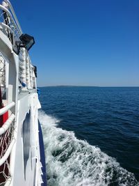 Cropped image of ferry sailing in sea against clear blue sky