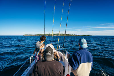 Rear view of men on boat in sea against sky