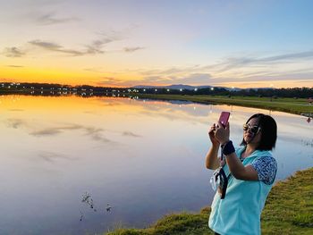 Rear view of woman photographing against sky during sunset