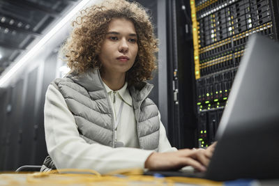 Engineer with curly hair working on laptop in server room