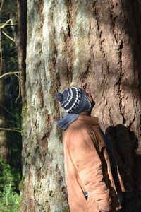 Rear view of woman standing against tree trunk