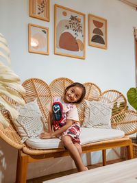 Happy little girl sitting on the rattan couch in a boho interior design.