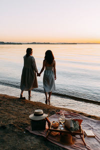 Happy woman friends relaxing on the beach with picnic on a sunny day