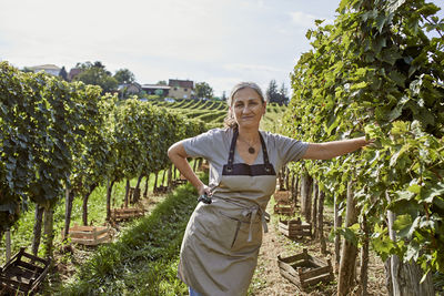 Smiling mature farmer standing with hand on hip in vineyard