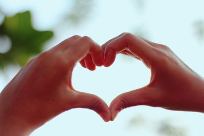 Cropped hands making heart shape against sky