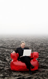 Businessman using laptop while sitting on landscape against sky