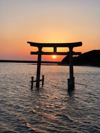 Silhouette wooden post in sea against sky during sunset