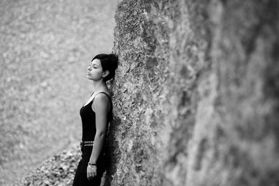 Side view of woman with eyes closed leaning on rock