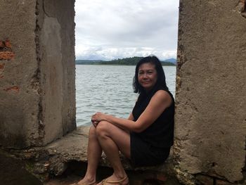 Portrait of smiling woman sitting on shore against sea